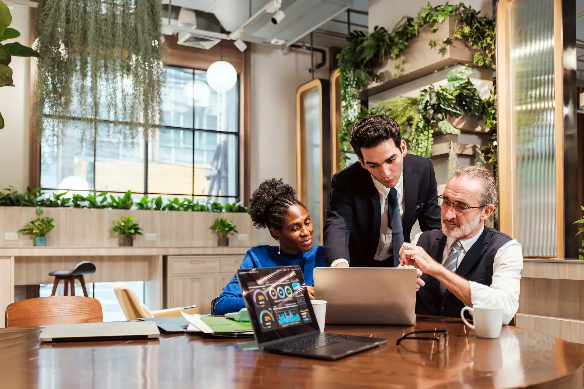 Three colleagues around a laptop in a plant-filled office, going through results together