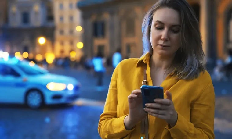 A woman checking her phone on a city street in the evening