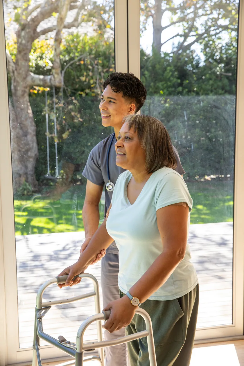A caregiver beside a resident with a walker, looking out through the glass doors to the garden