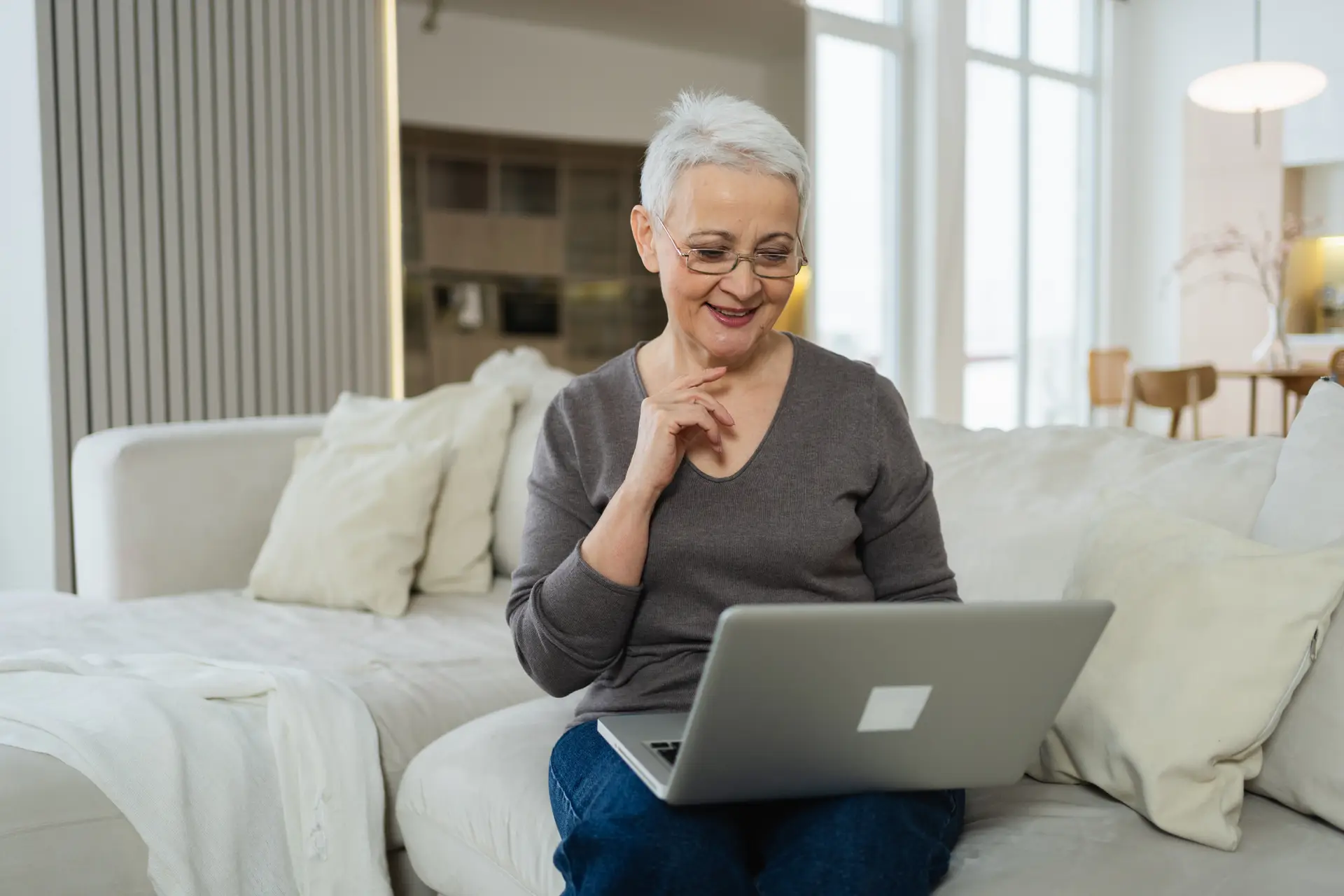An older woman on a sofa reading on a laptop