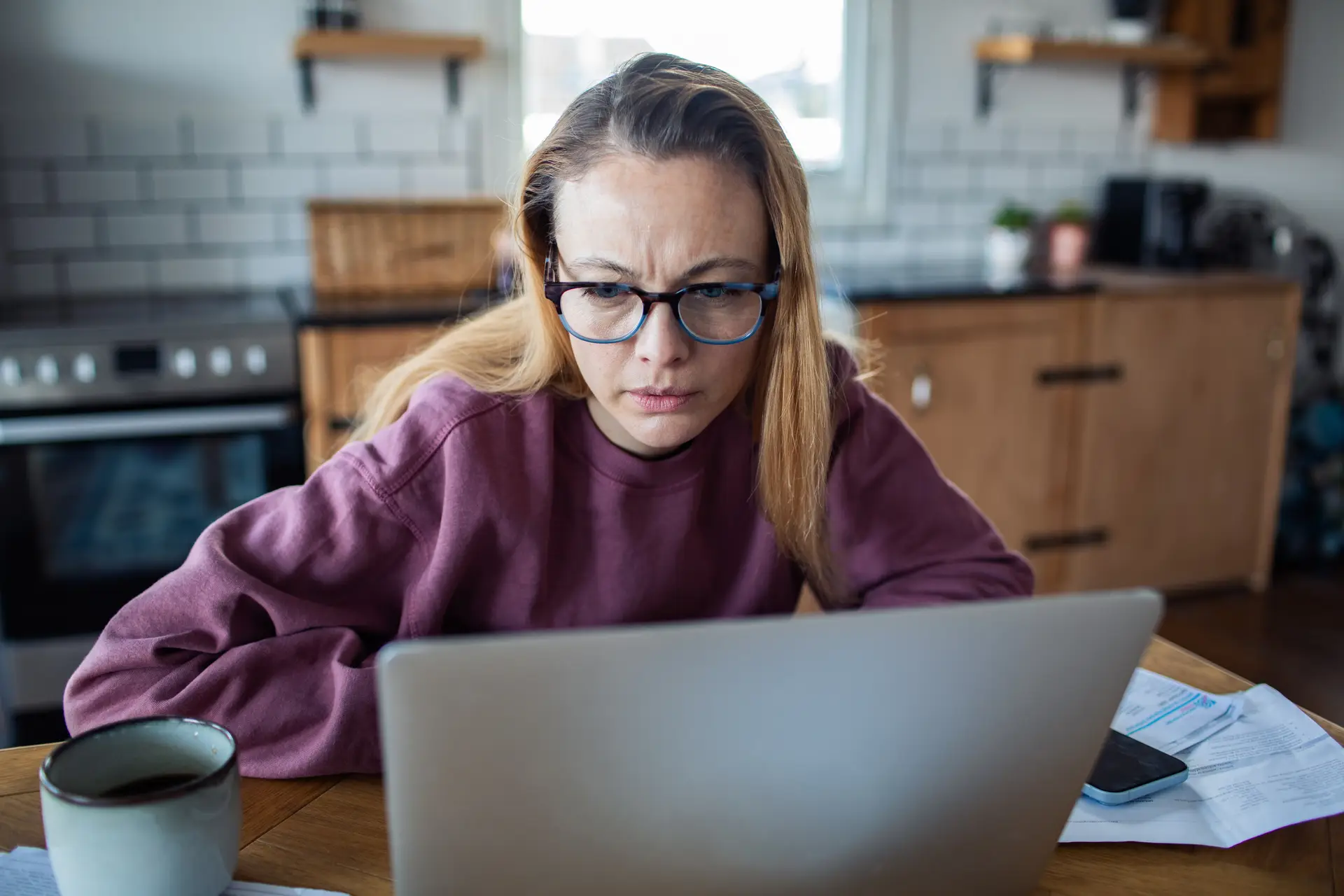A woman concentrating on a laptop at a kitchen table